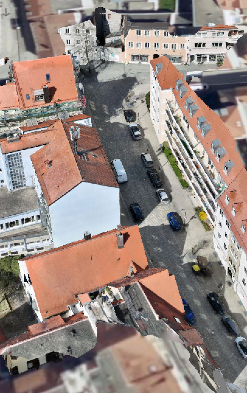 Bird's eye view of narrow European street with orange-roofed buildings and parked cars.