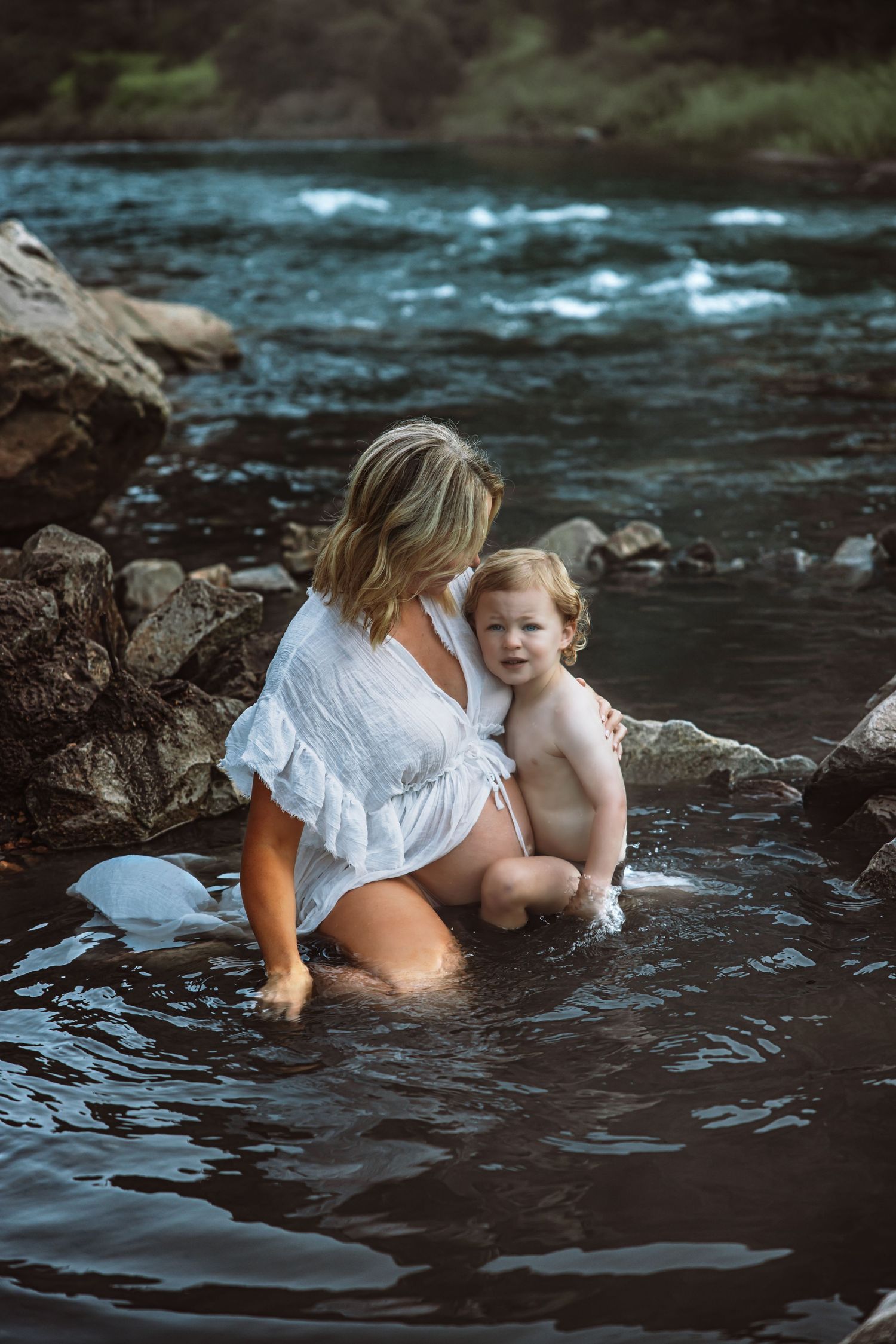 Intimate moment captured at rocky riverbank during water photoshoot.