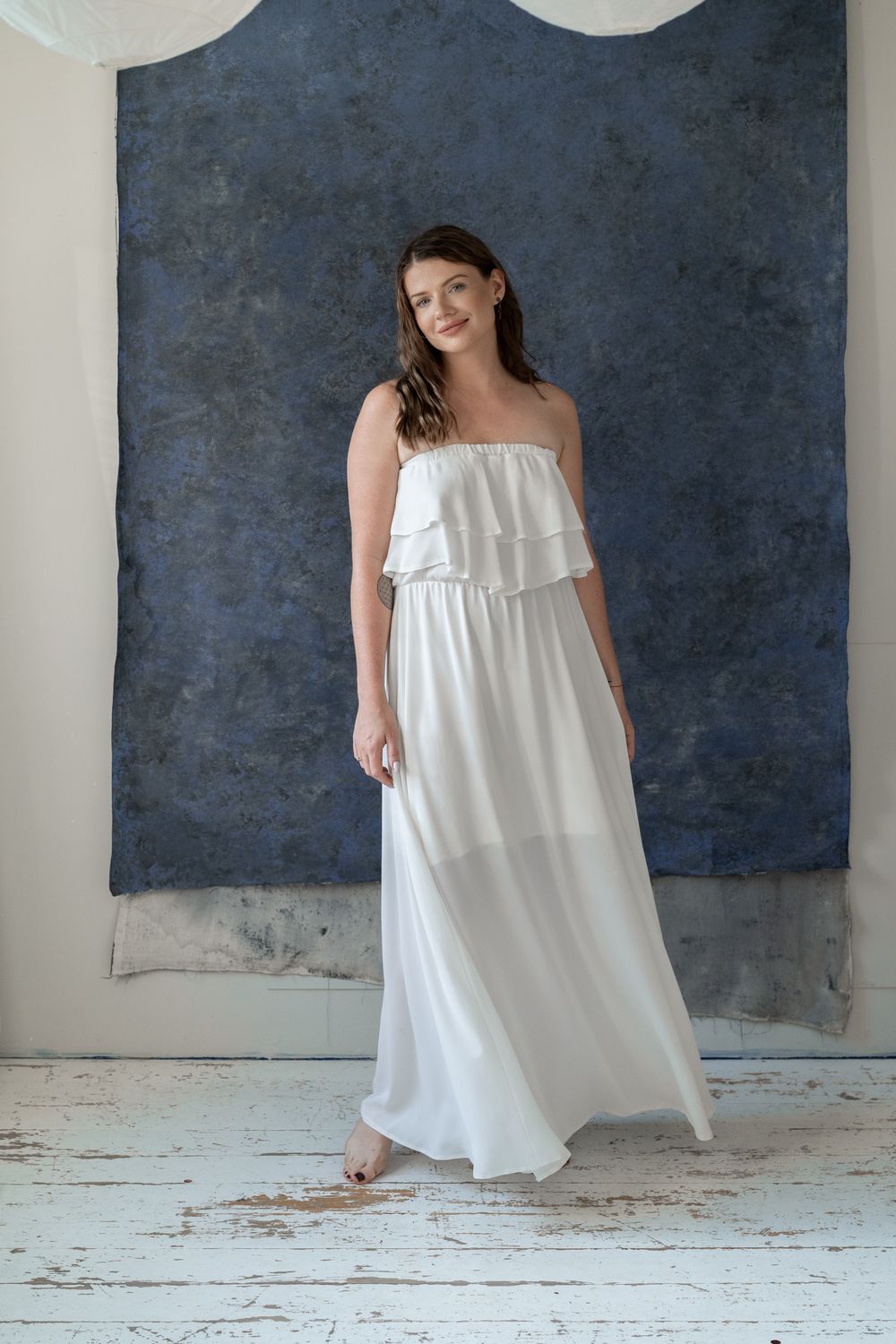 Full-length portrait of person wearing white strapless maxi dress in studio setting.