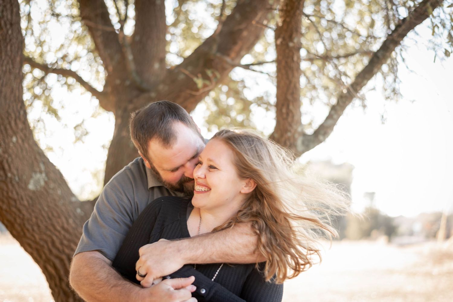 Family shares intimate moments under a large tree during sunset photo session.