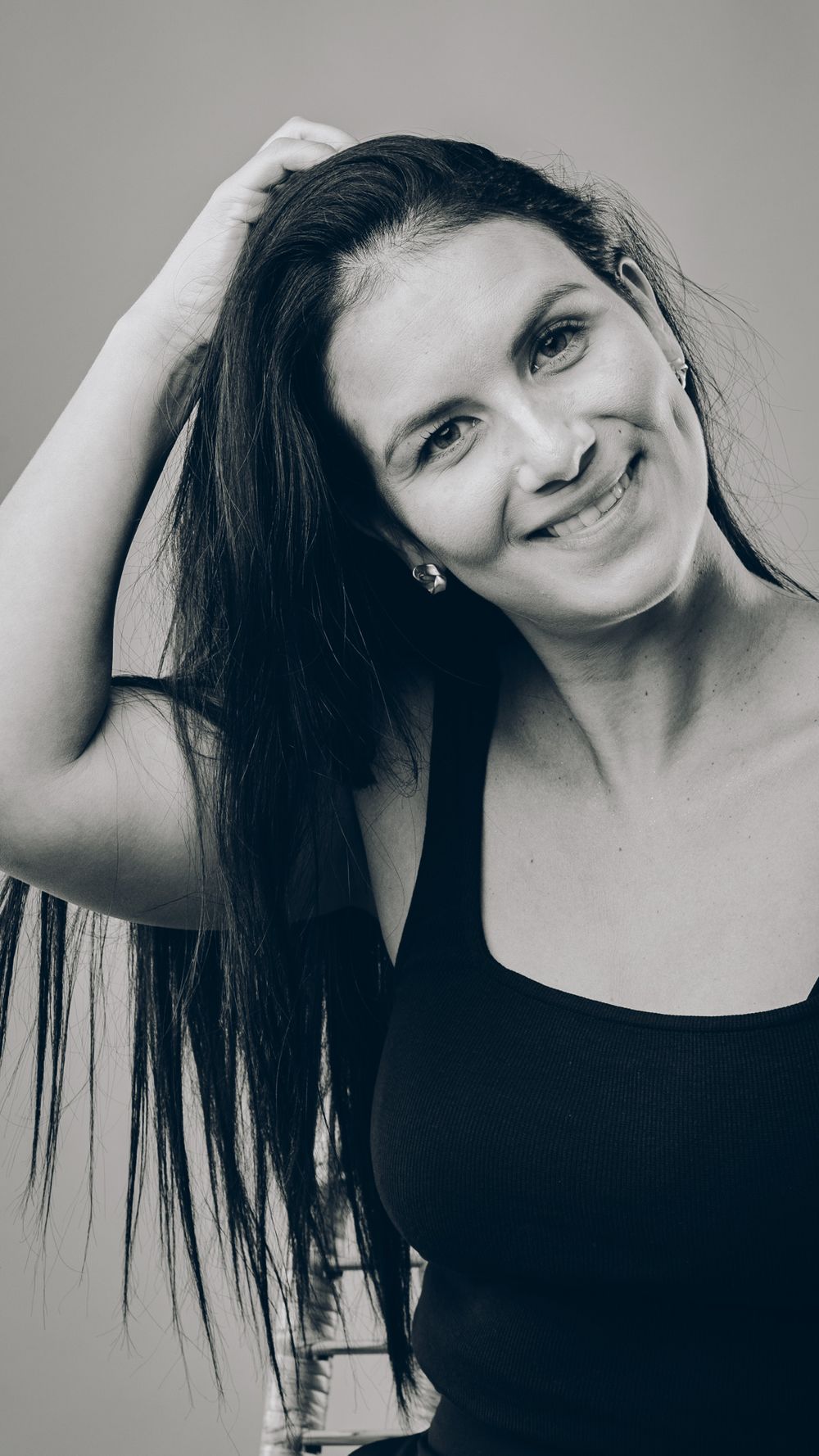 Black and white portrait of someone with long dark hair in a tank top smiling naturally.