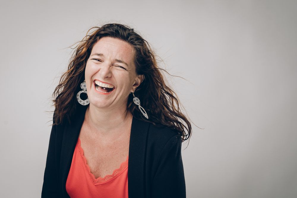 Portrait of woman with flowing hair laughing against neutral background.