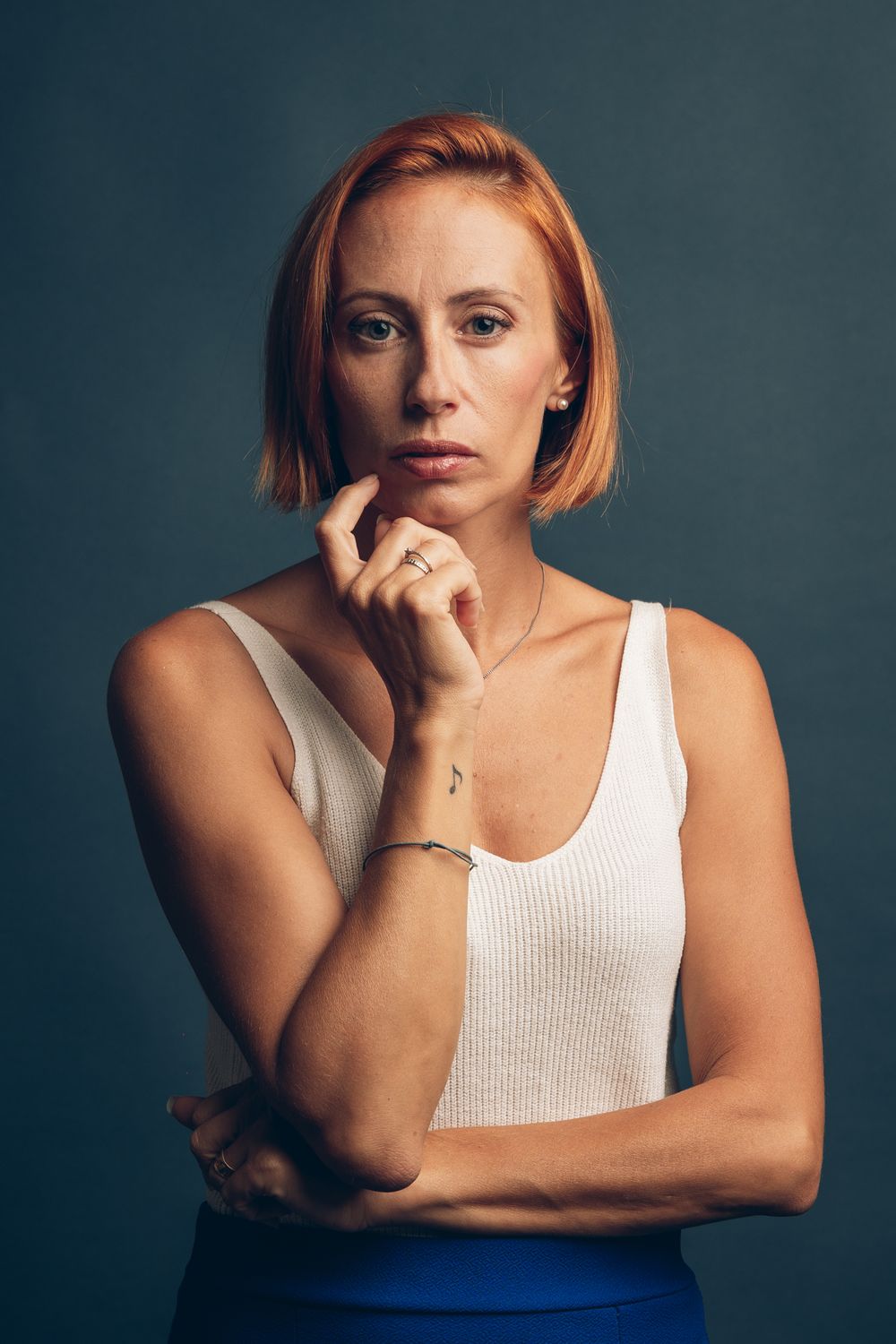 Contemplative studio portrait of someone in a white tank top against a dark background.
