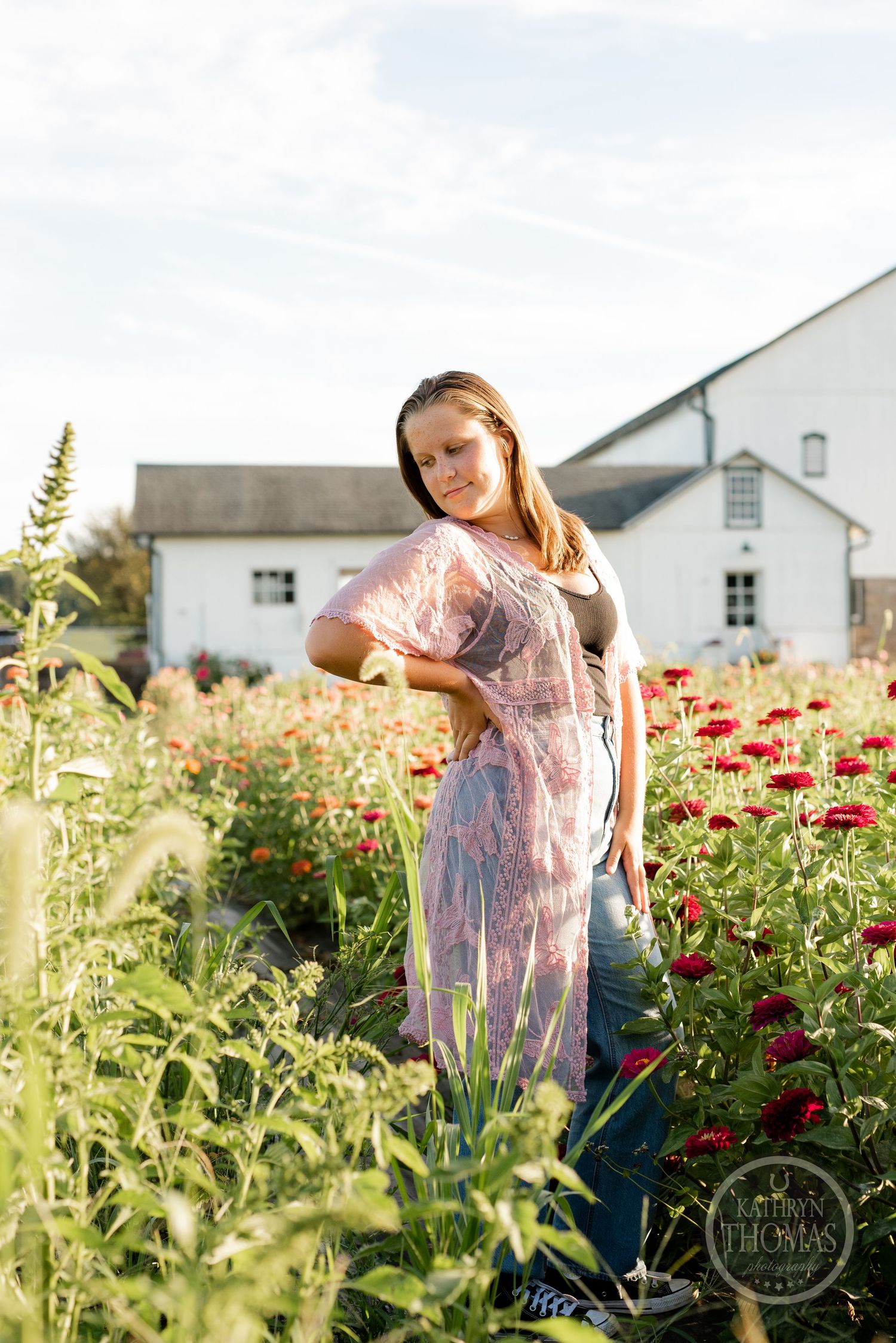 A golden hour portrait in a flowering field with a white farmhouse in the background.