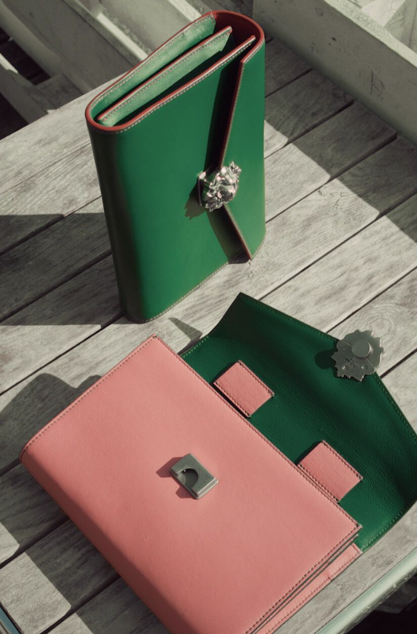 Pink and green leather notebooks with decorative clasps on a wooden surface.