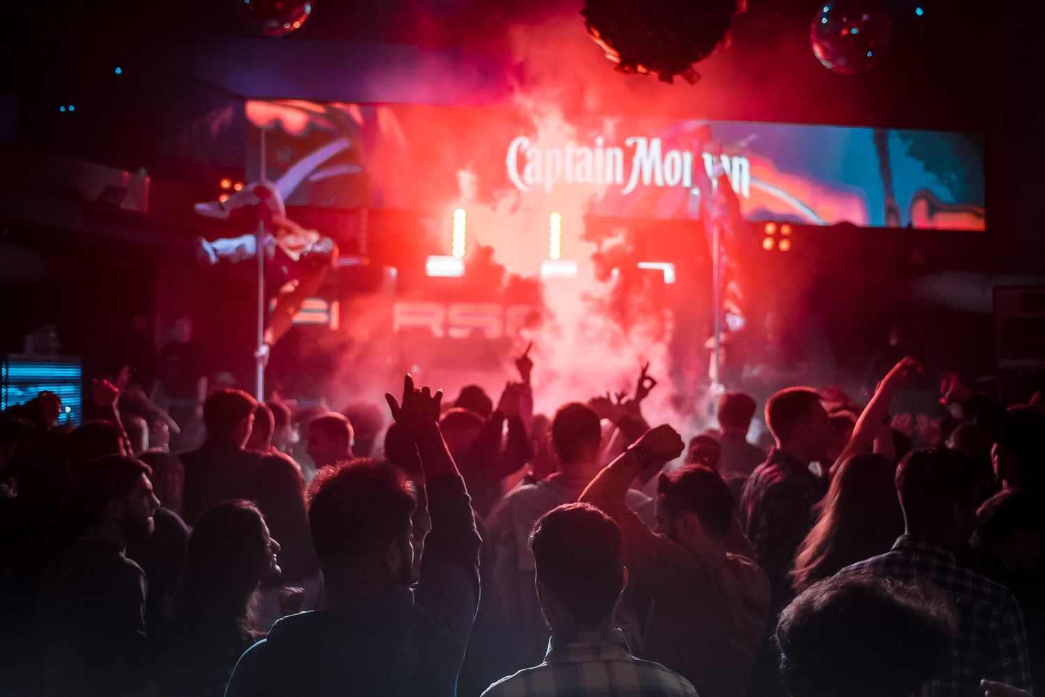 Nightclub crowd silhouetted against bright red stage lighting during live performance.