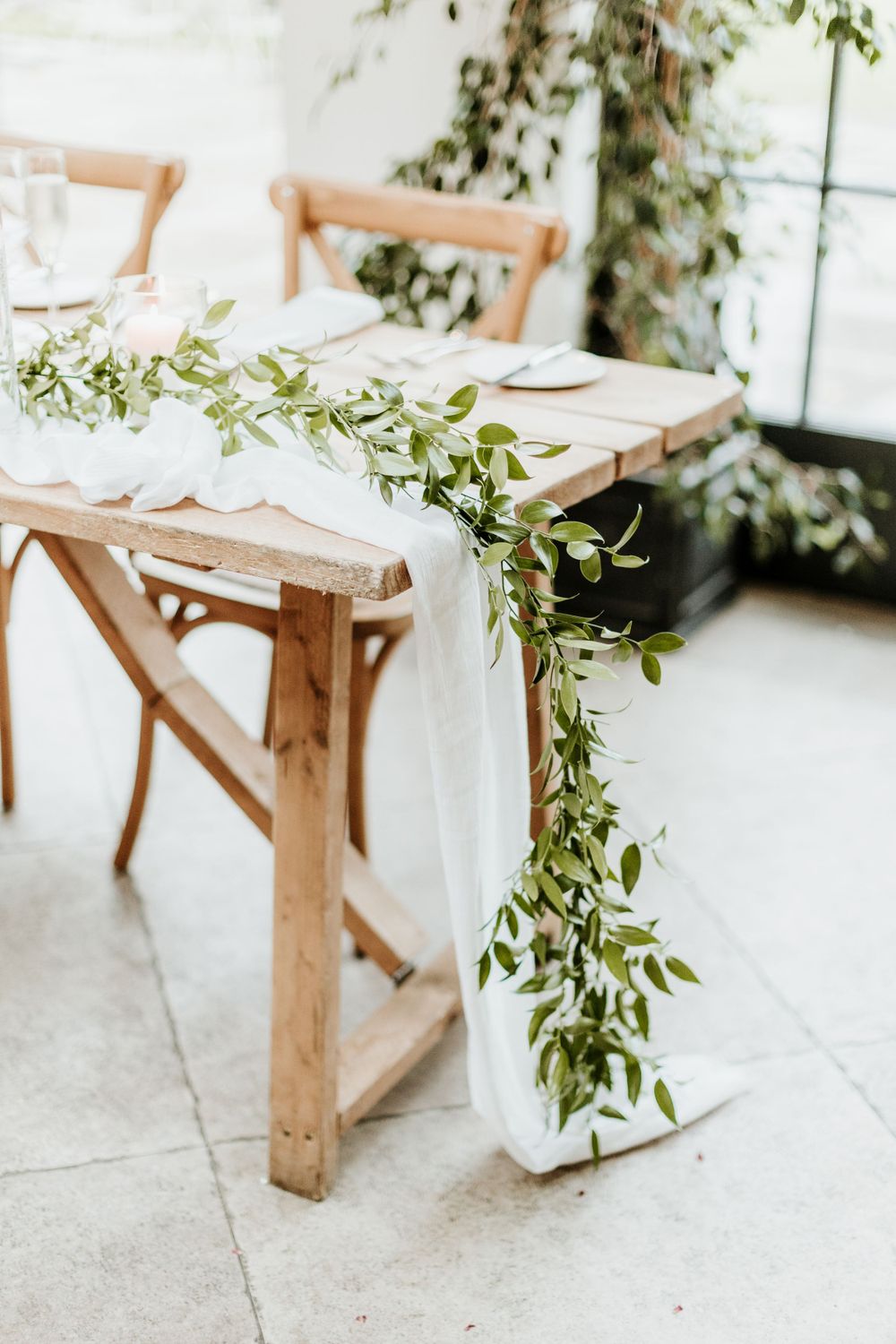 An elegant table setting with white linens and a flowing greenery garland runner.