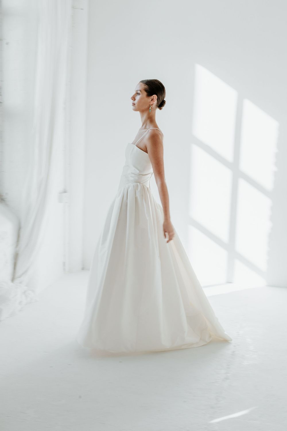 Minimalist white wedding gown with fitted bodice and flowing skirt photographed in a bright white studio.
