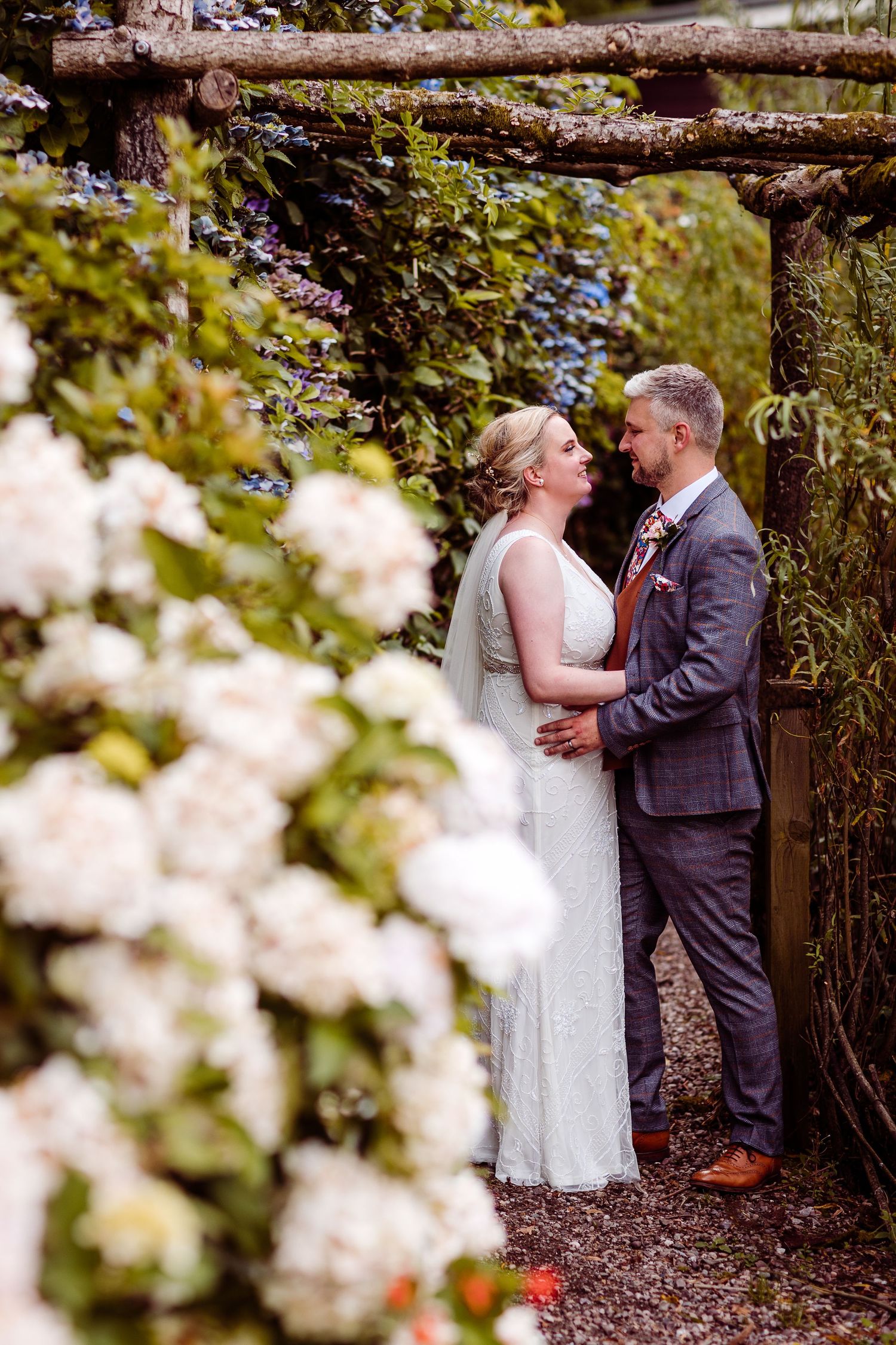A romantic moment captured in a garden archway surrounded by blooming white flowers.