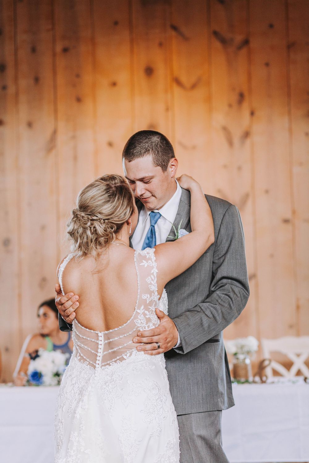 Bride and groom share emotional first dance in front of warm wooden barn wall.