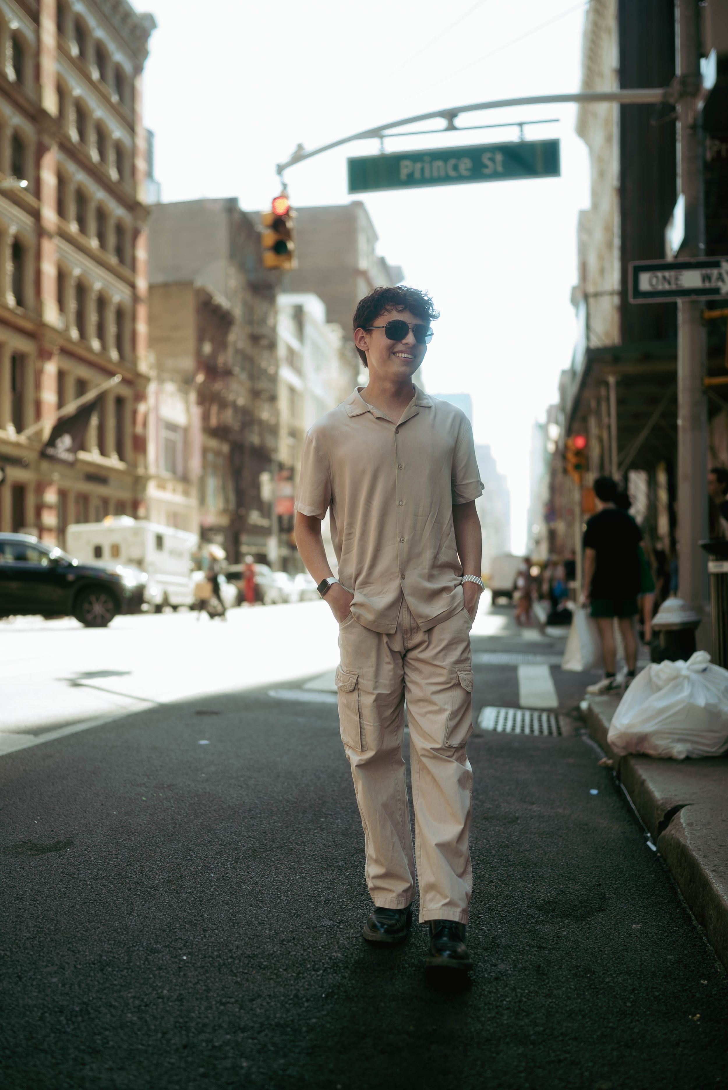 A person in monochromatic clothing walks down a city street with a traffic light visible.