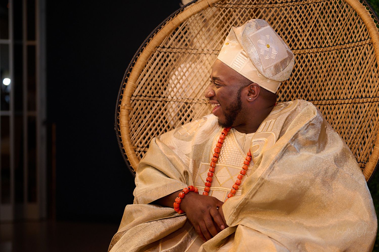 A person in traditional Nigerian attire sits in a decorative peacock chair against a dark background.