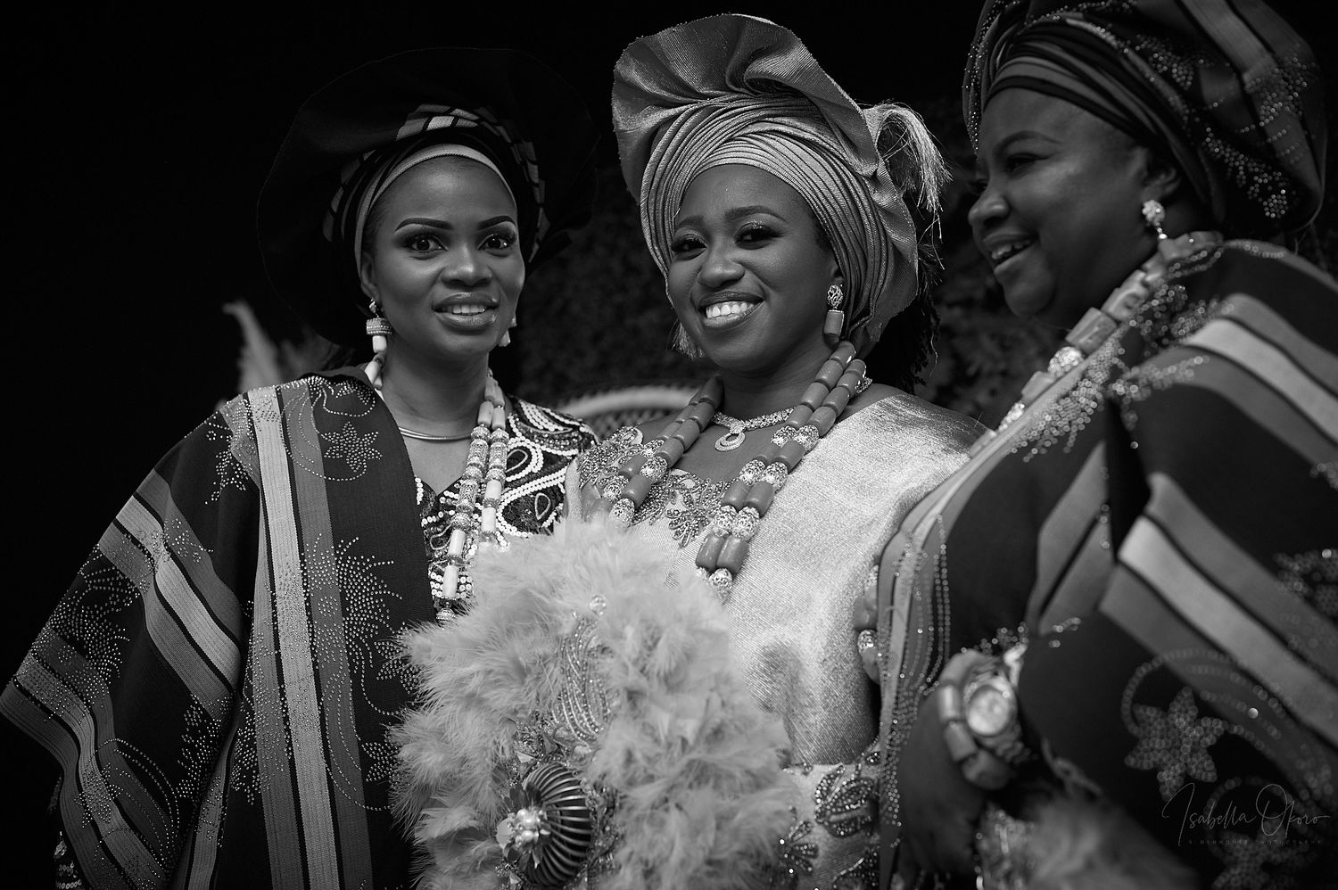 Three women in traditional African attire laughing together during a celebration.