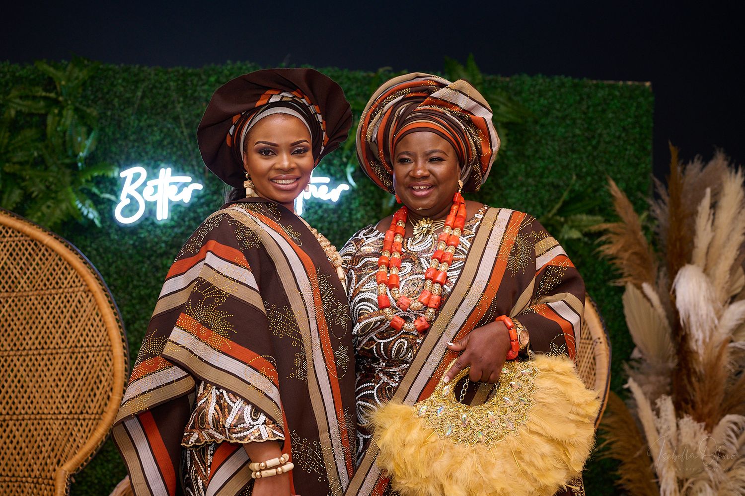Two people in vibrant African formal wear pose against a backdrop with neon lighting.