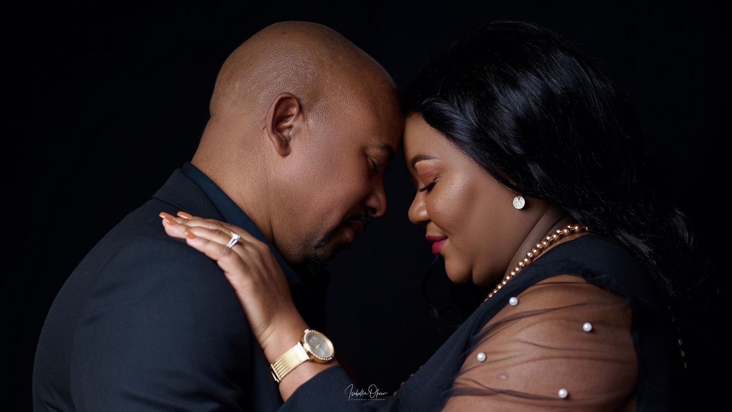 Couple in formal wear embracing in romantic studio portrait with brown and orange tones.
