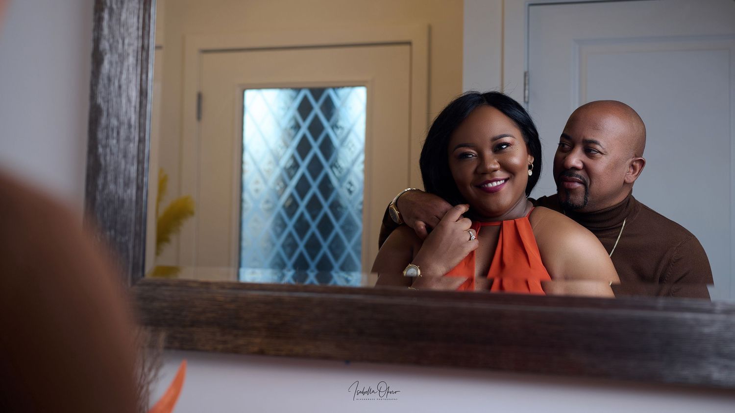 Mirror reflection captures couple in orange and brown attire sharing joyful moment.