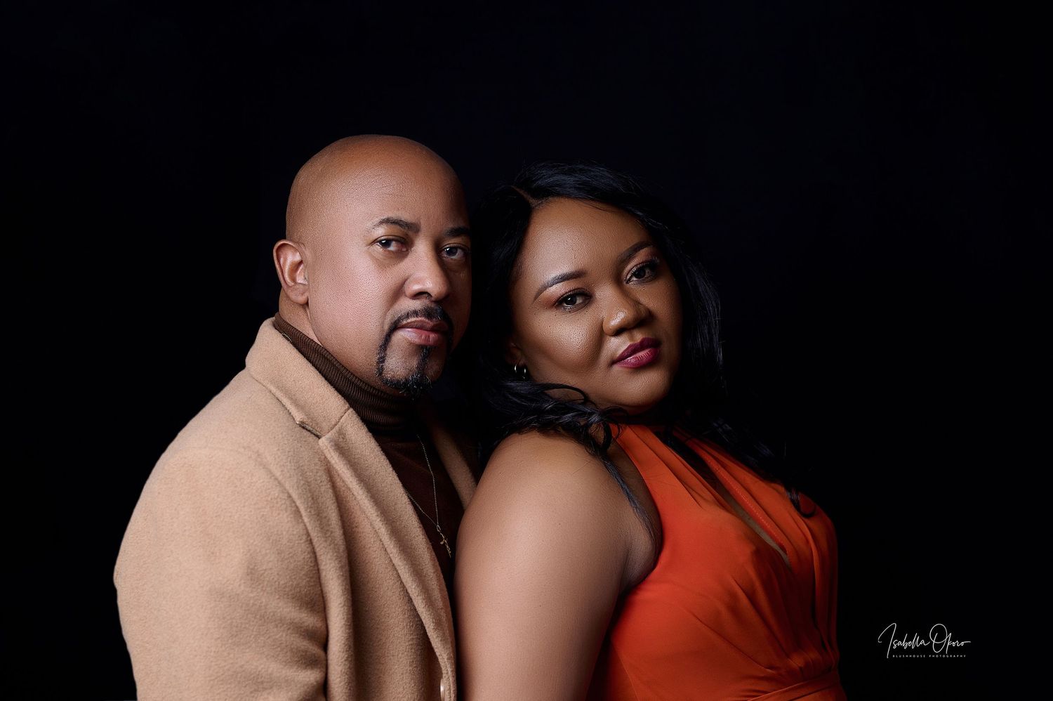 Stylish couple poses in tan blazer and orange dress for romantic photoshoot.
