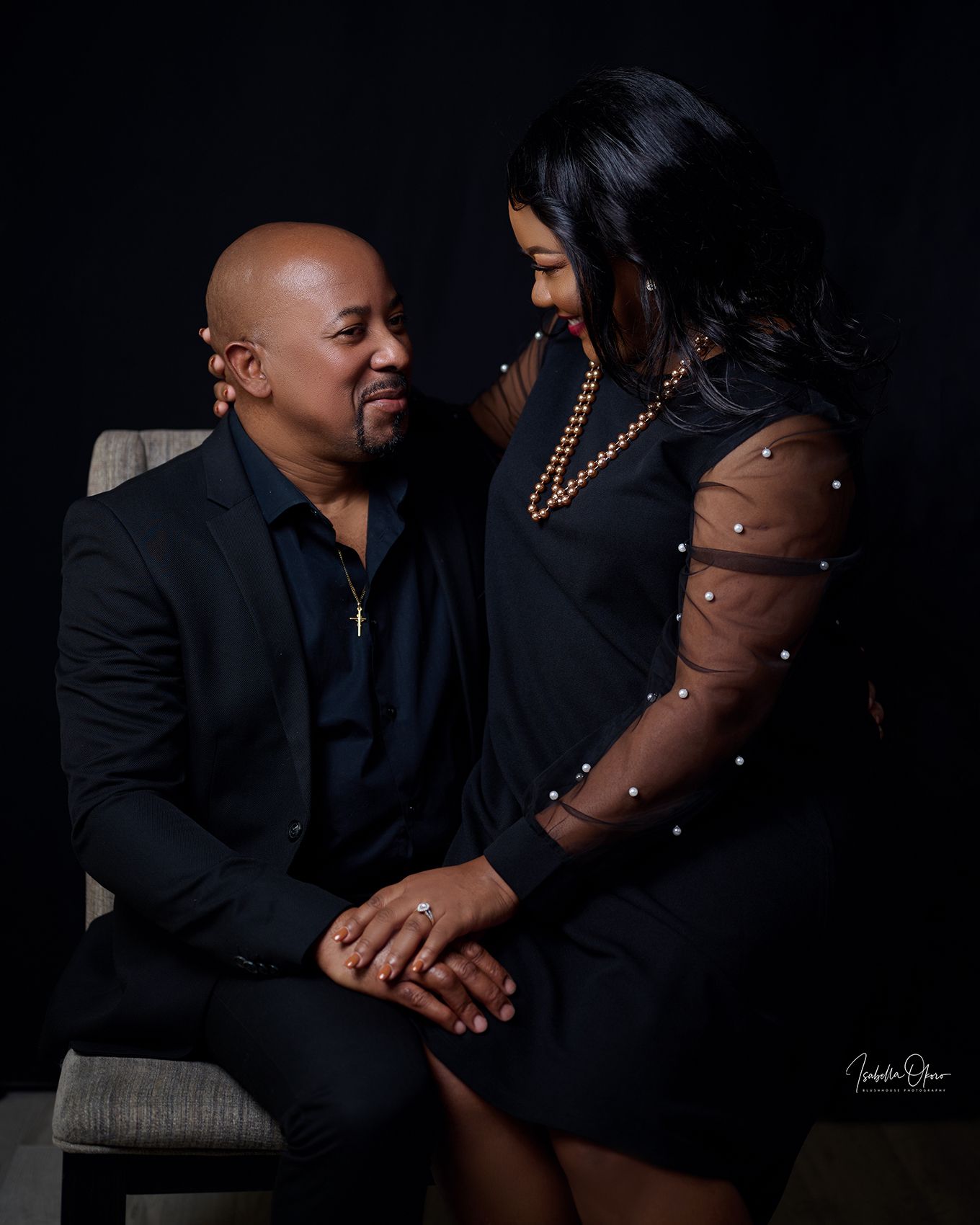 Romantic couple in black attire sharing an intimate moment against dark backdrop.