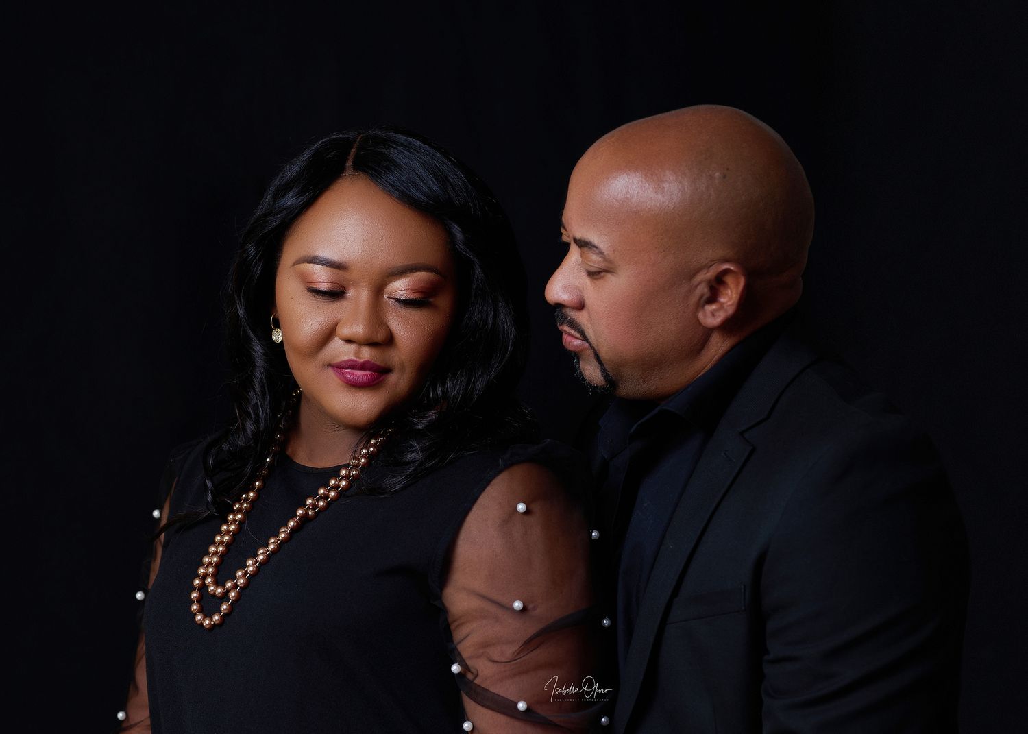 Intimate couple portrait in black attire against dark background.