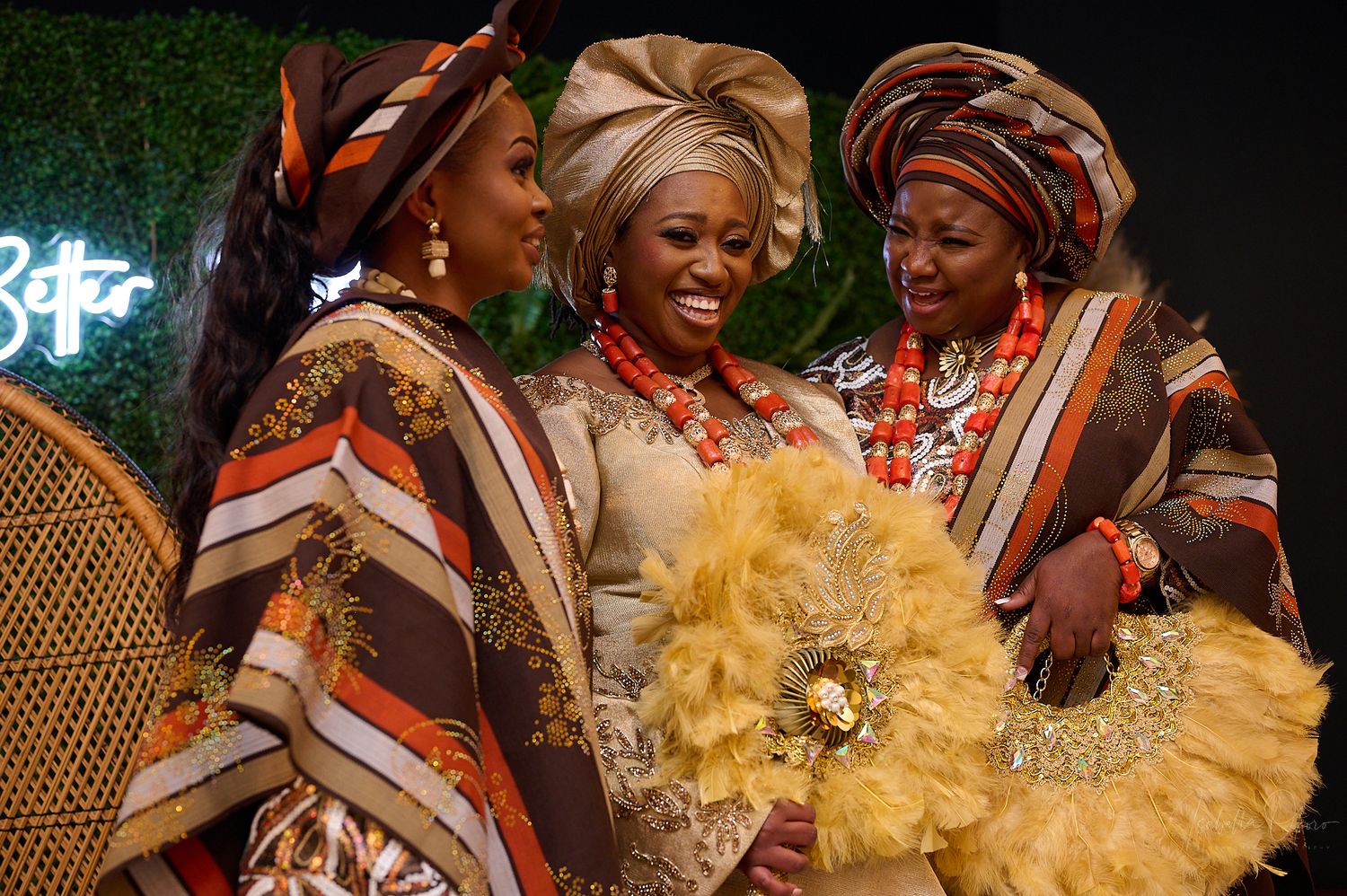 Three people in colorful traditional African dress pose with yellow ceremonial fans.