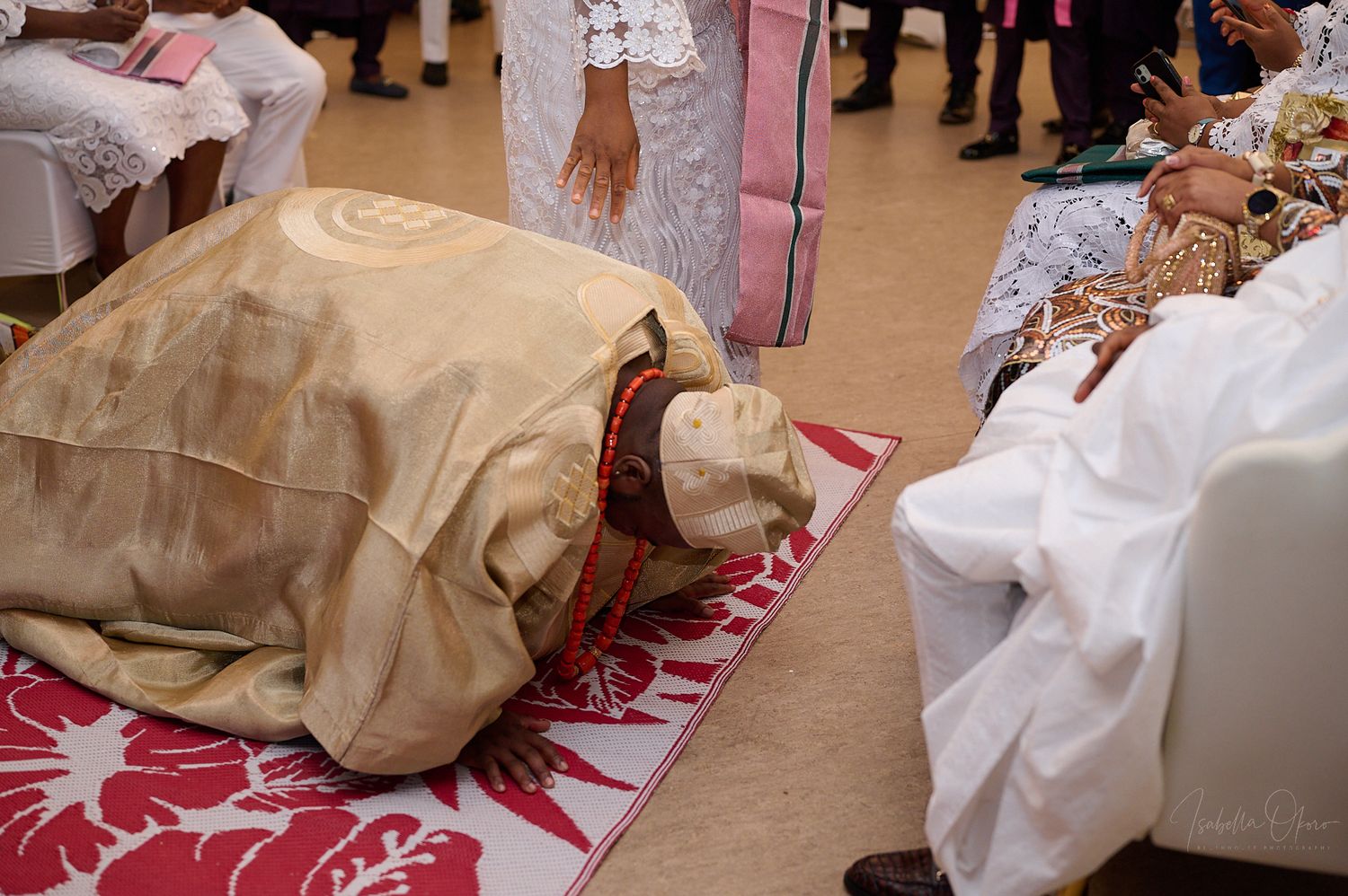 Traditional prostration ceremony with person bowing on decorative red and white mat.