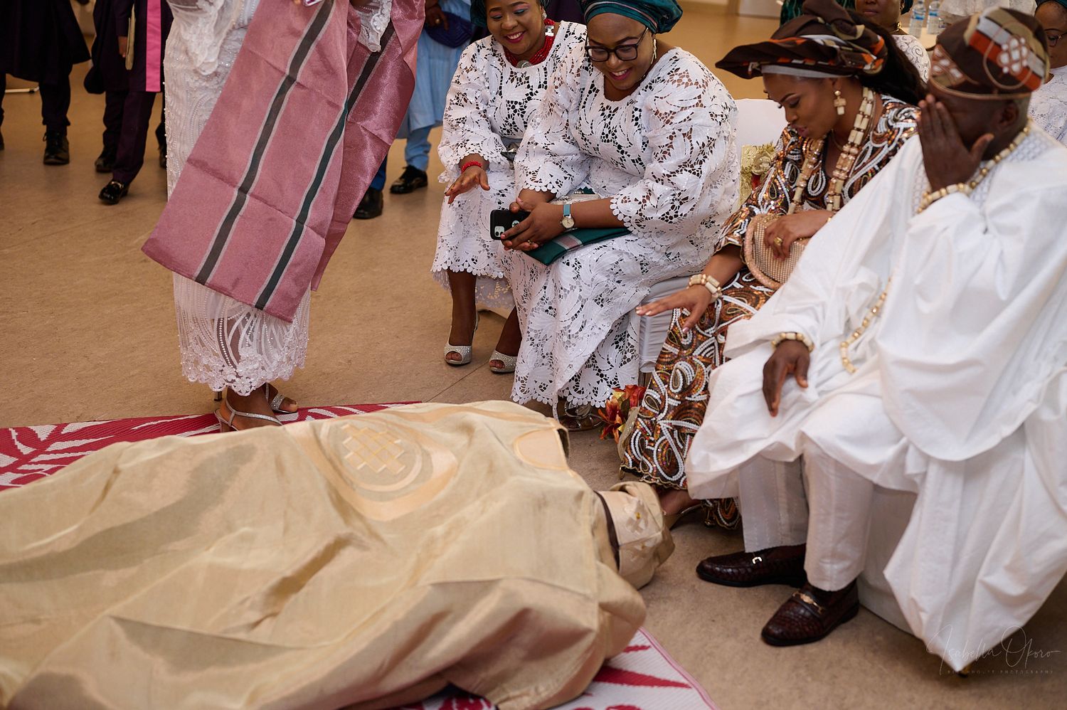 Cultural ceremony showing traditional prostration ritual with observers in white and patterned attire.