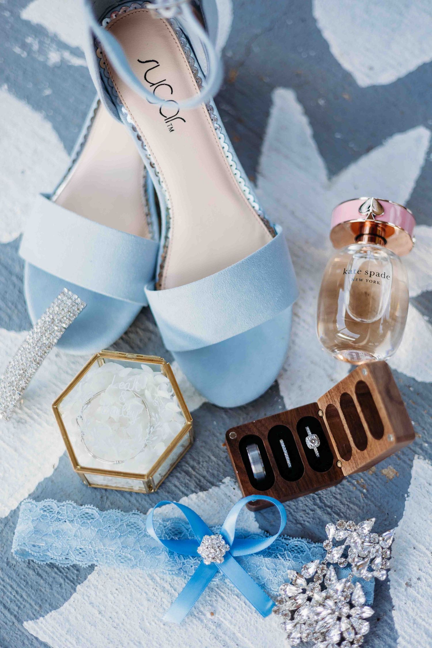 Wedding accessories including crystal-embellished shoes and perfume bottles arranged on blue surface.