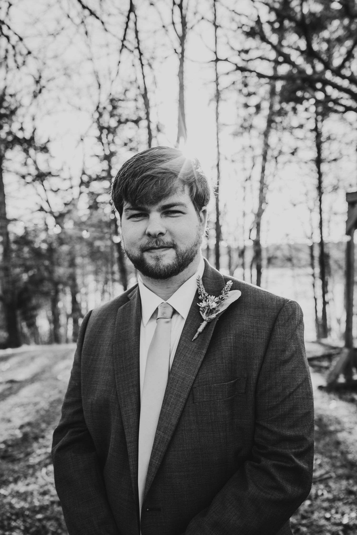 Black and white portrait of a person wearing a suit and tie in a wooded setting.