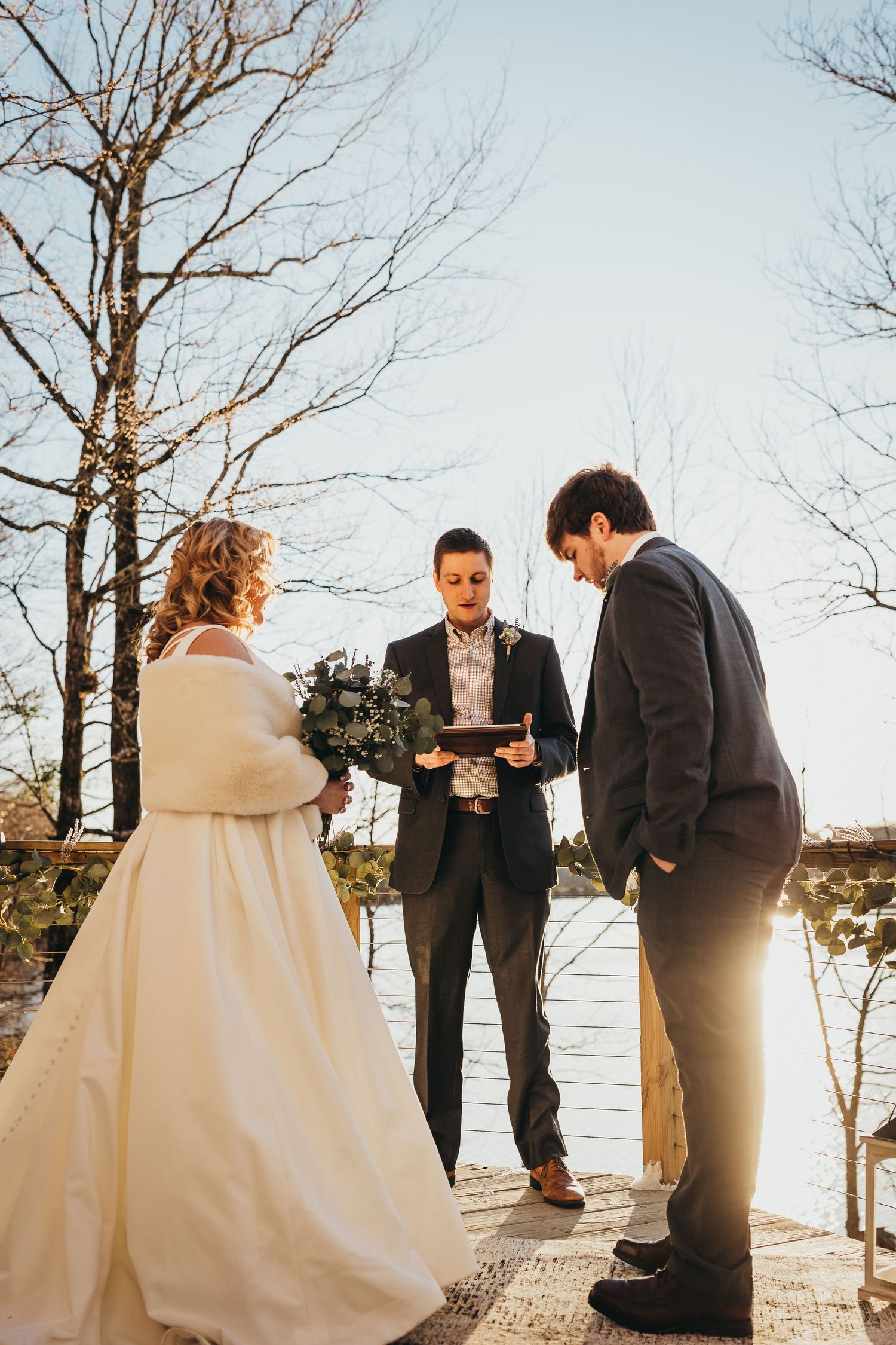 Wedding party gathered on a wooden deck by the water during sunset.