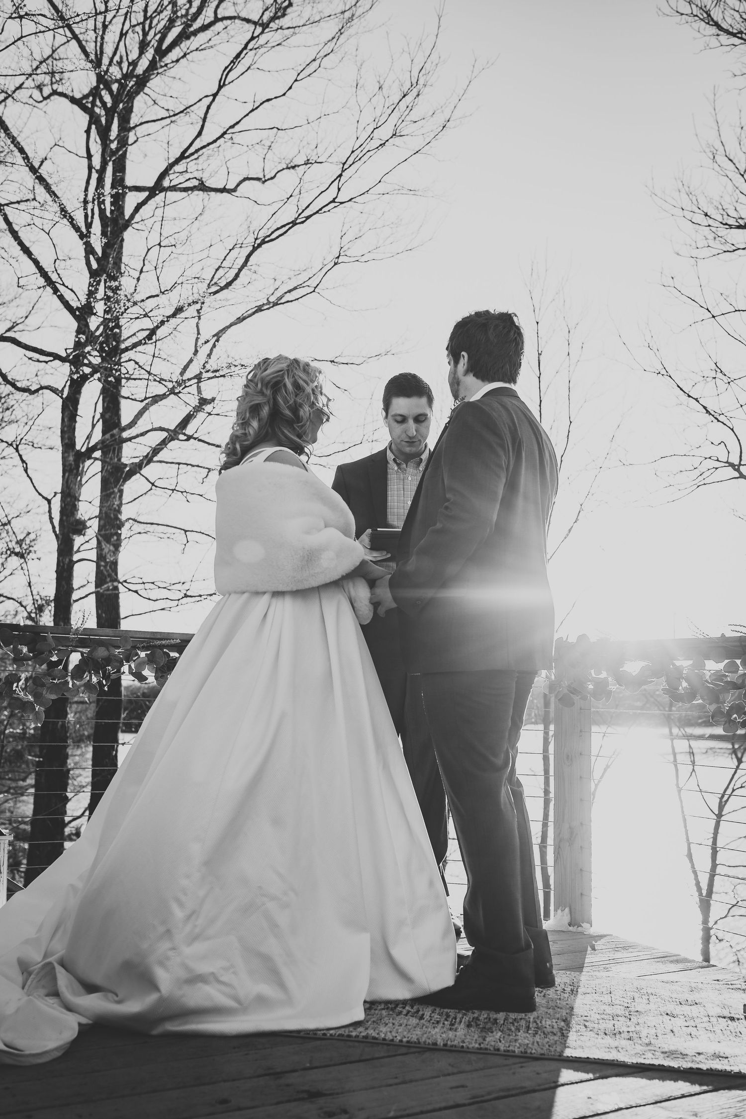 Black and white photos capture a romantic wedding scene against bare winter trees and sunlit water.