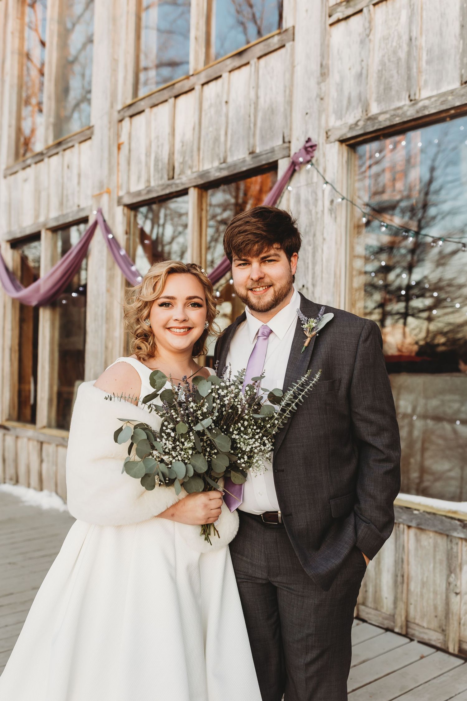 Wedding couple poses with bouquet on rustic wooden deck during sunset ceremony.