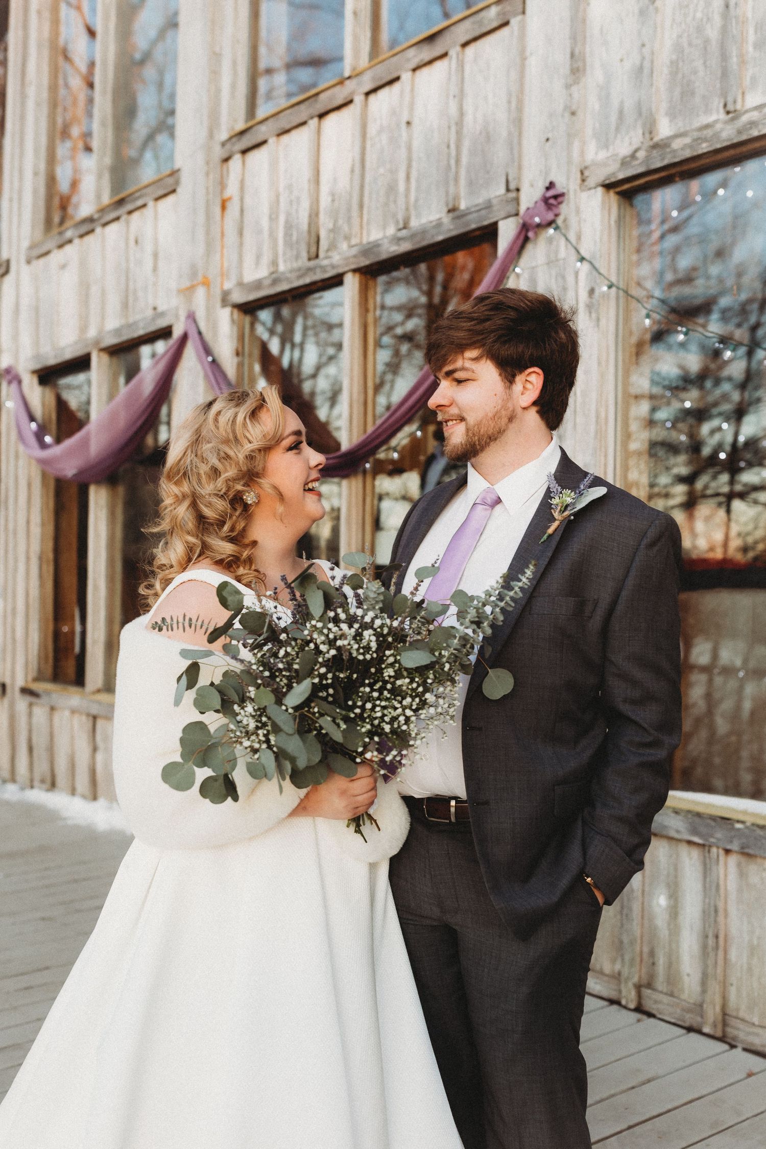 Wedding couple shares intimate moment in front of rustic wooden barn wall.