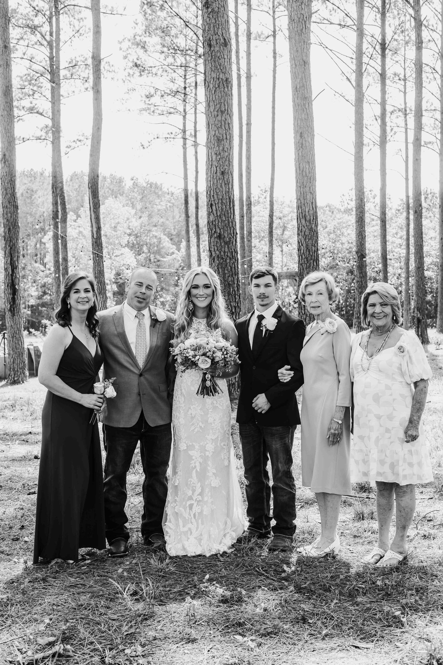 Large wedding party lined up for formal photo in black and white forest setting.