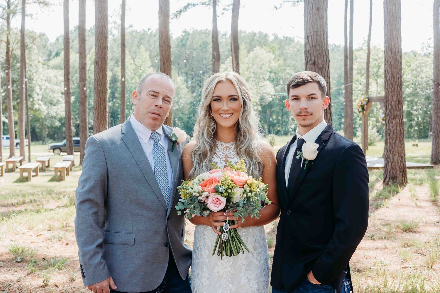 Wedding photo of small group in formal attire standing among tall pine trees.
