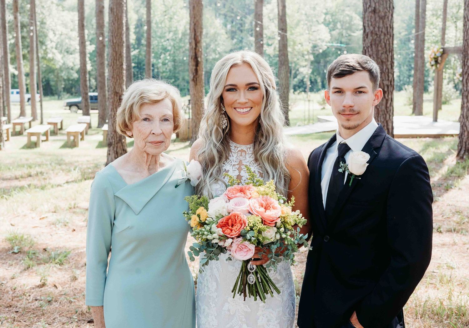 Wedding party members gather for photos in a sunlit forest setting.