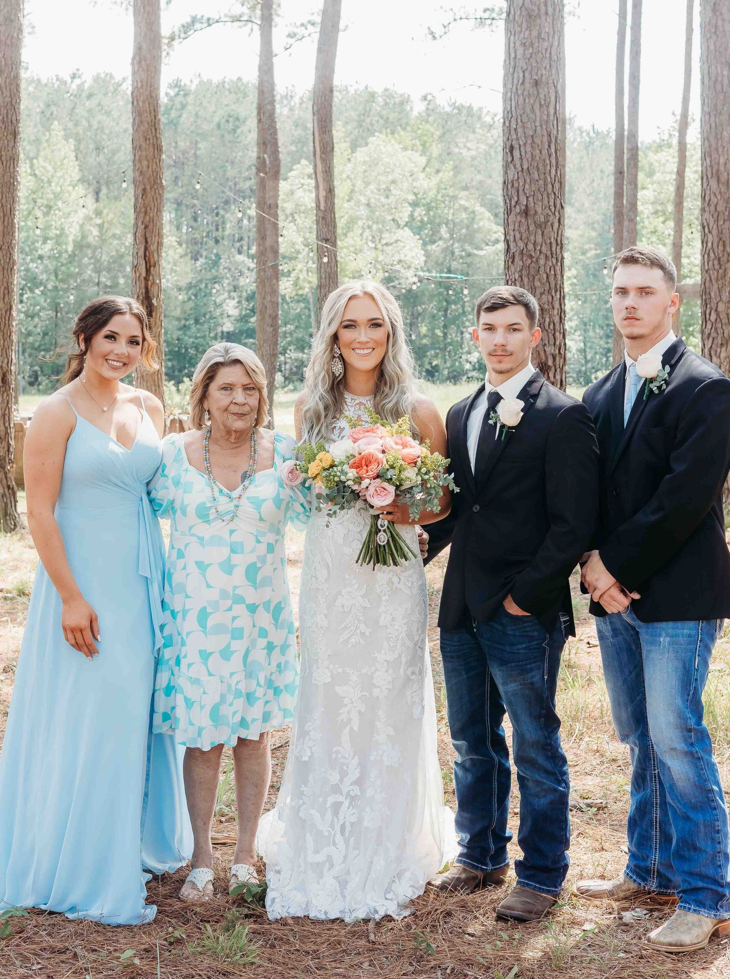 Wedding party members in blue and white attire pose together in a forest setting.