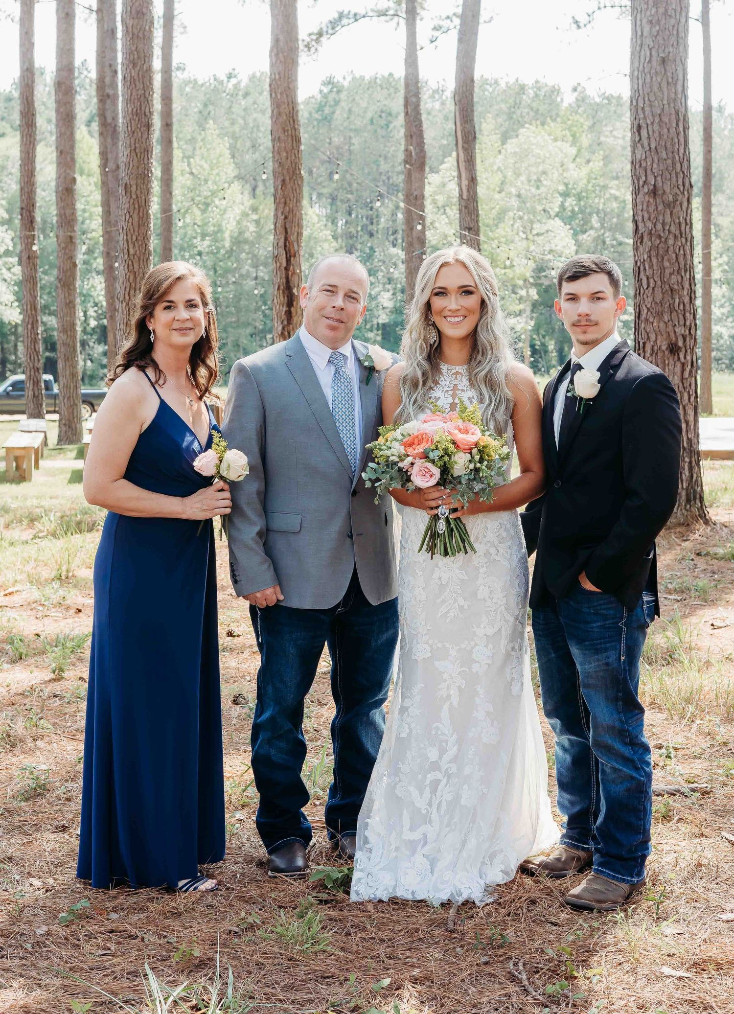 Wedding party poses among tall pine trees in a forest setting with bridesmaids in navy dresses.