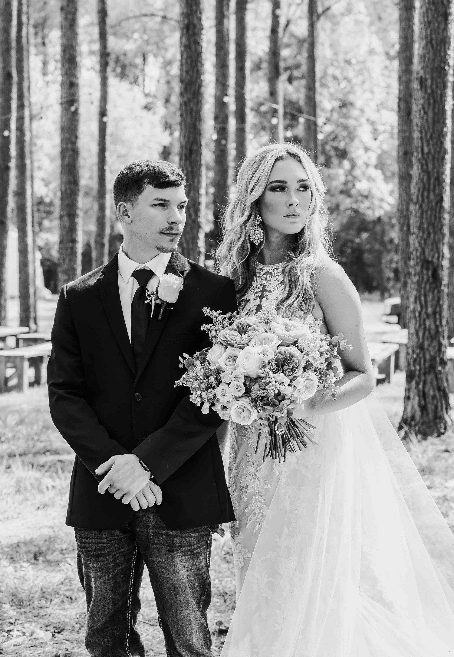 Black and white wedding photo of a couple walking through a pine forest.