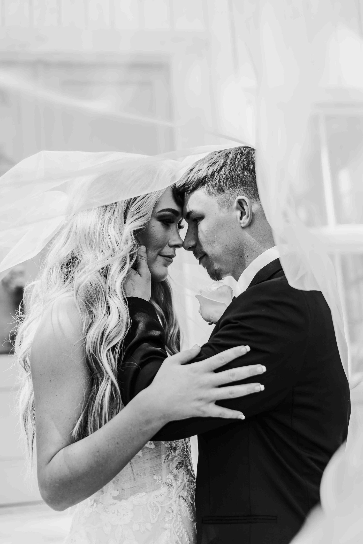 Monochrome close-up of newlyweds sharing an intimate moment with bride's hand on groom's chest.