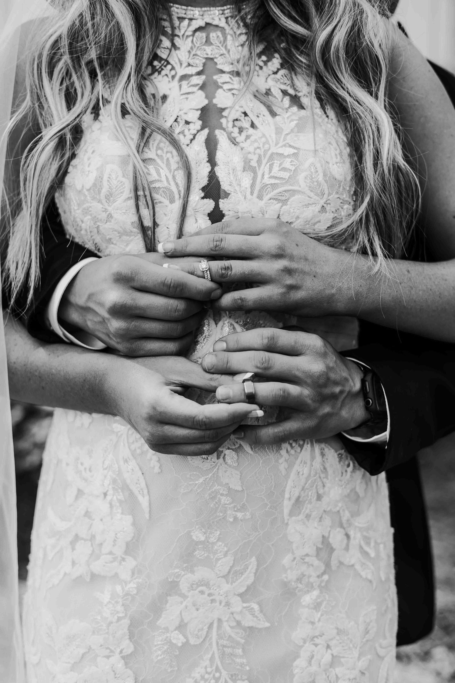 Detail shots of hands against white lace wedding dress showing delicate rings and textures.