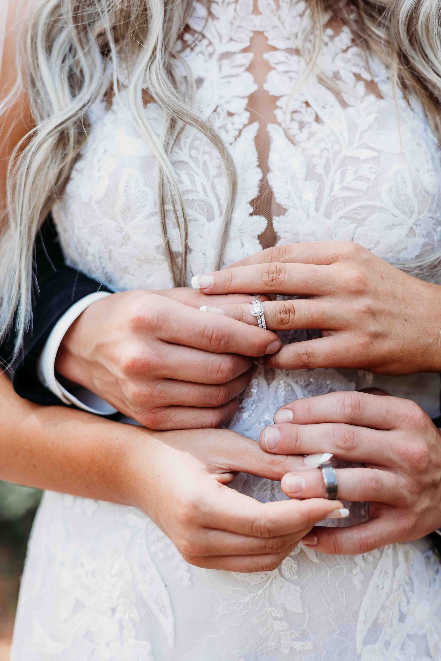 Close-up detail shots of hands with wedding rings against white floral lace dress fabric.