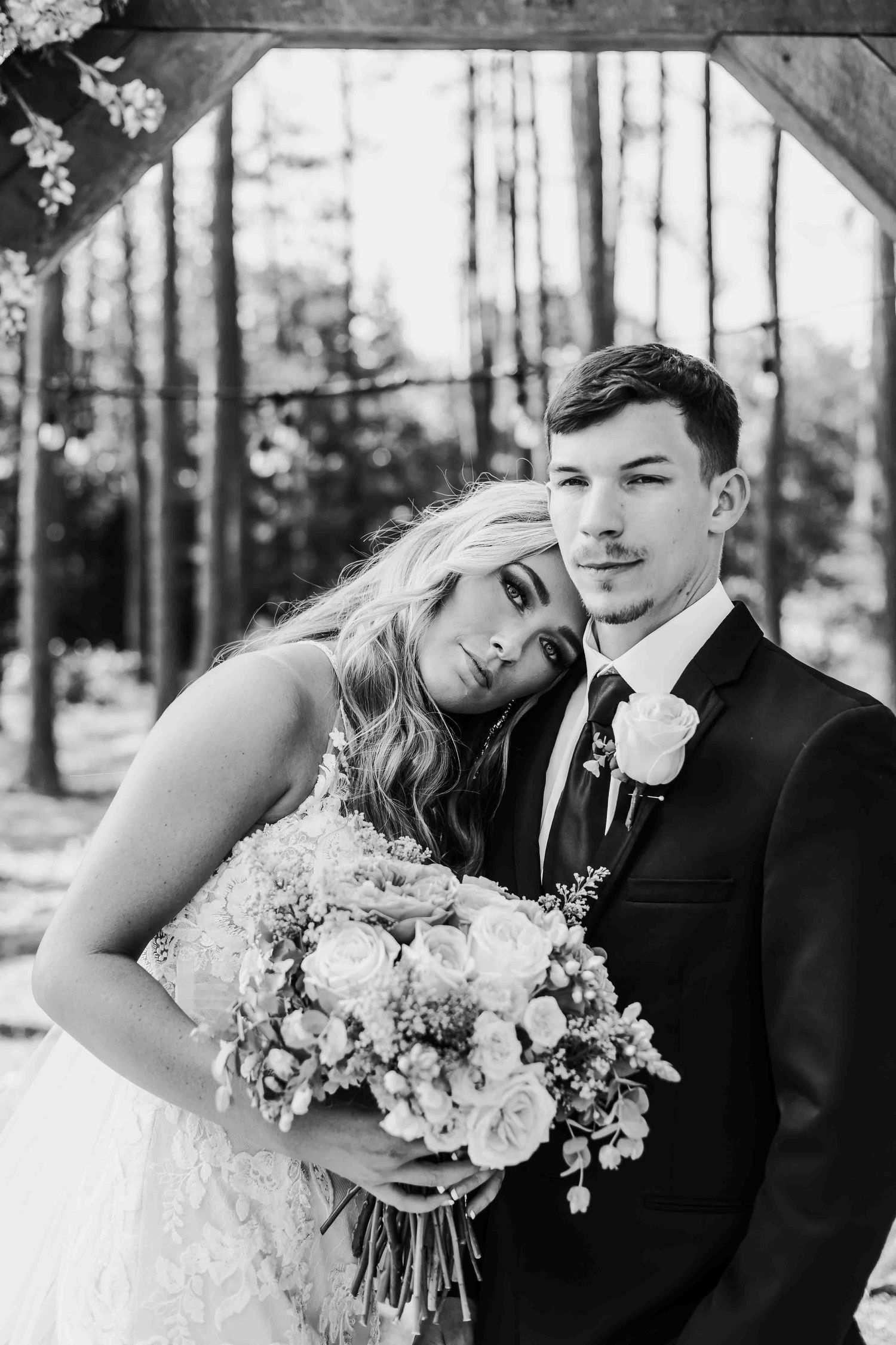 Romantic wedding portraits in forest setting featuring elegant bouquet with roses and greenery.
