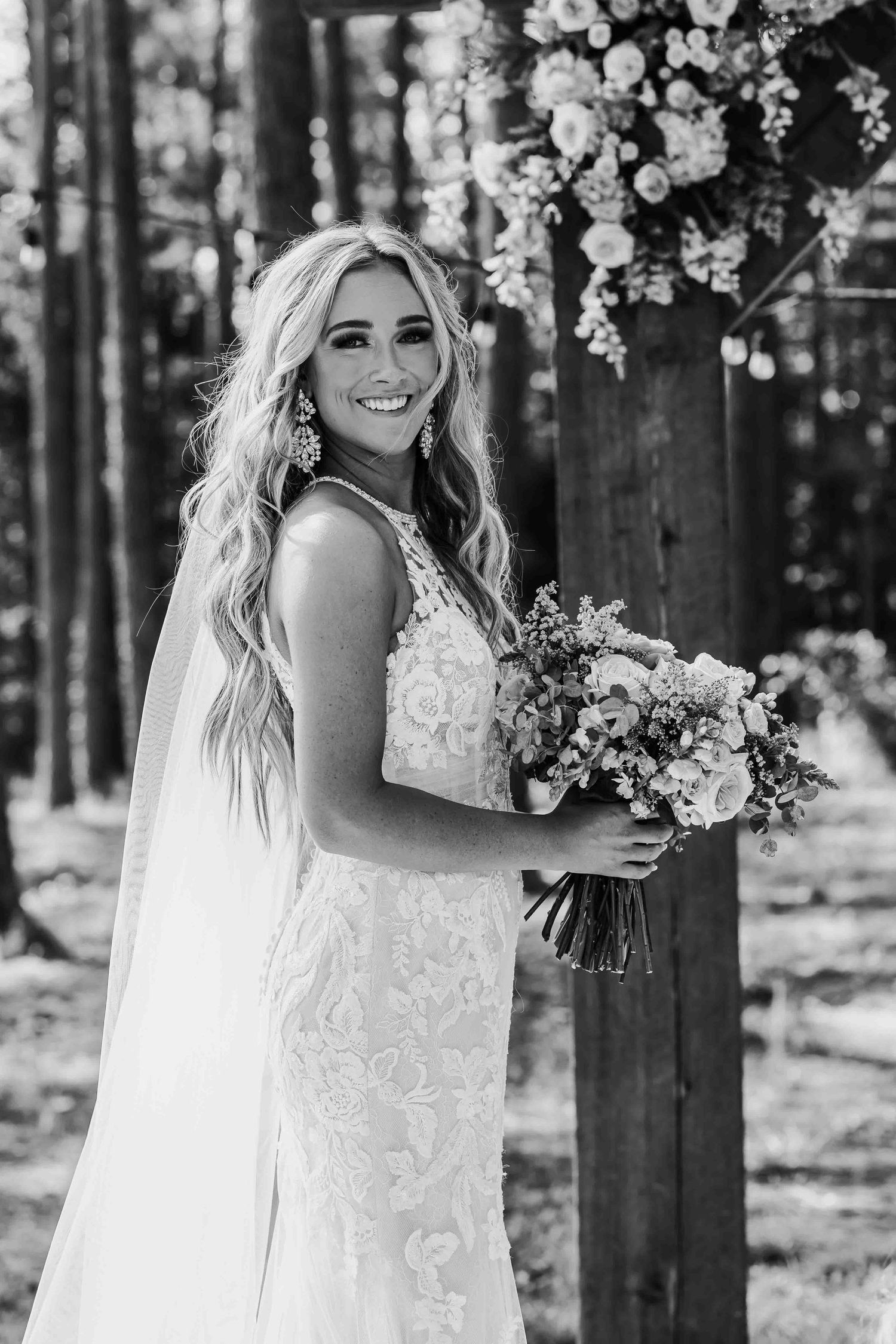 Black and white bridal portraits among trees with delicate lace dress and floral bouquet.