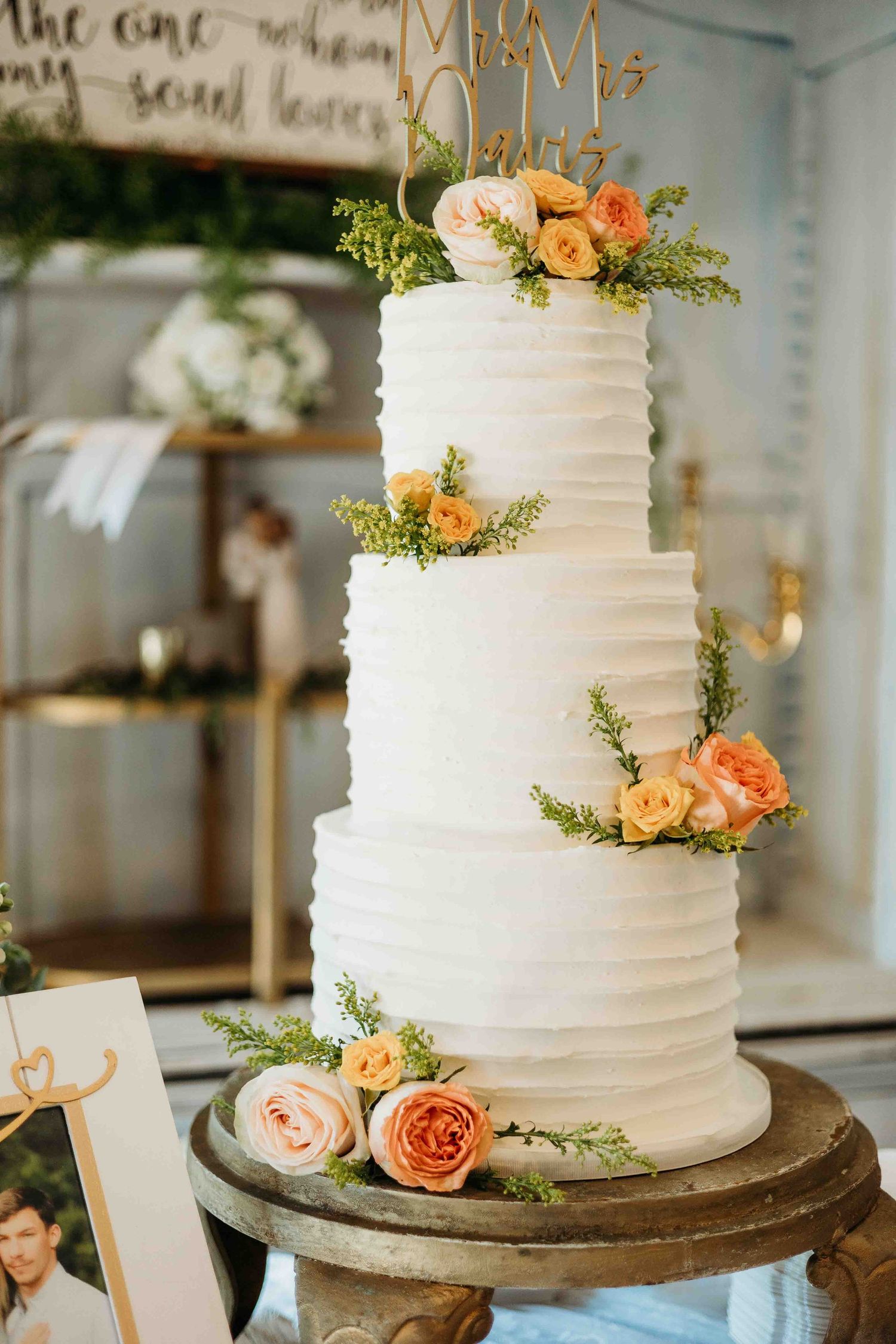 White tiered wedding cakes adorned with peach roses and greenery on rustic wooden stands.