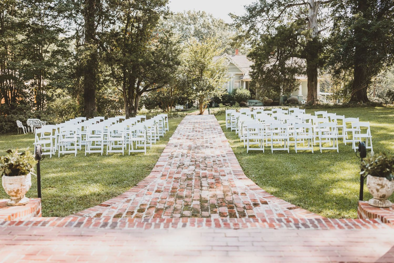 White ceremony chairs arranged in neat rows along a brick pathway for an outdoor wedding.