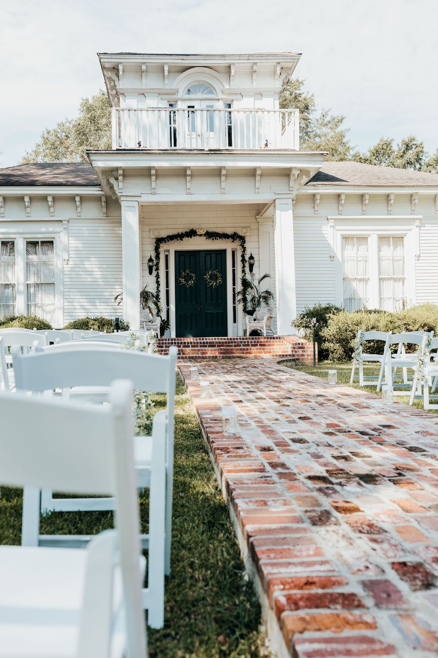 A classic white wedding venue with brick walkway and white ceremony chairs set up outdoors.