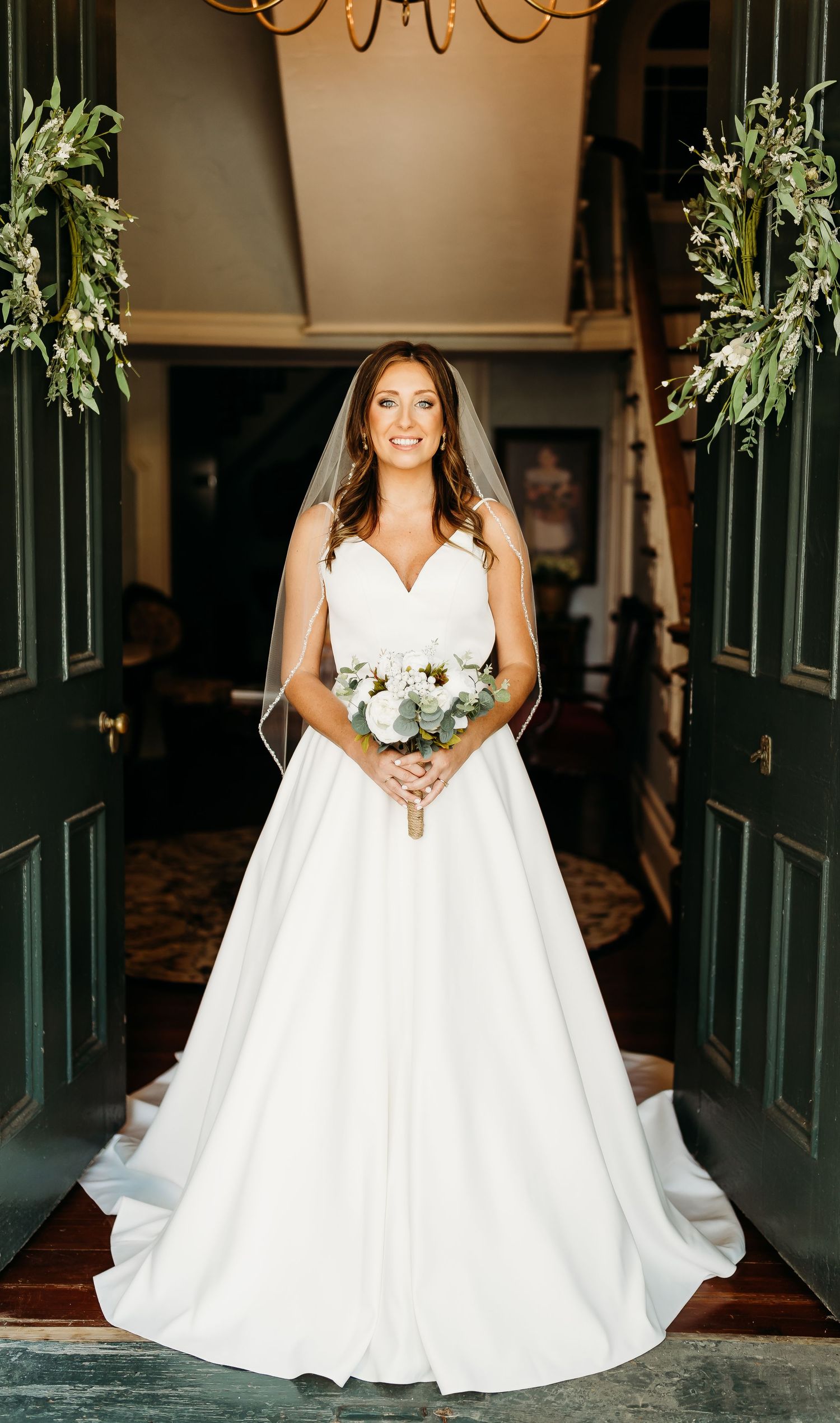 Radiant bride in a white V-neck ball gown holds a bouquet while standing in a grand entrance.
