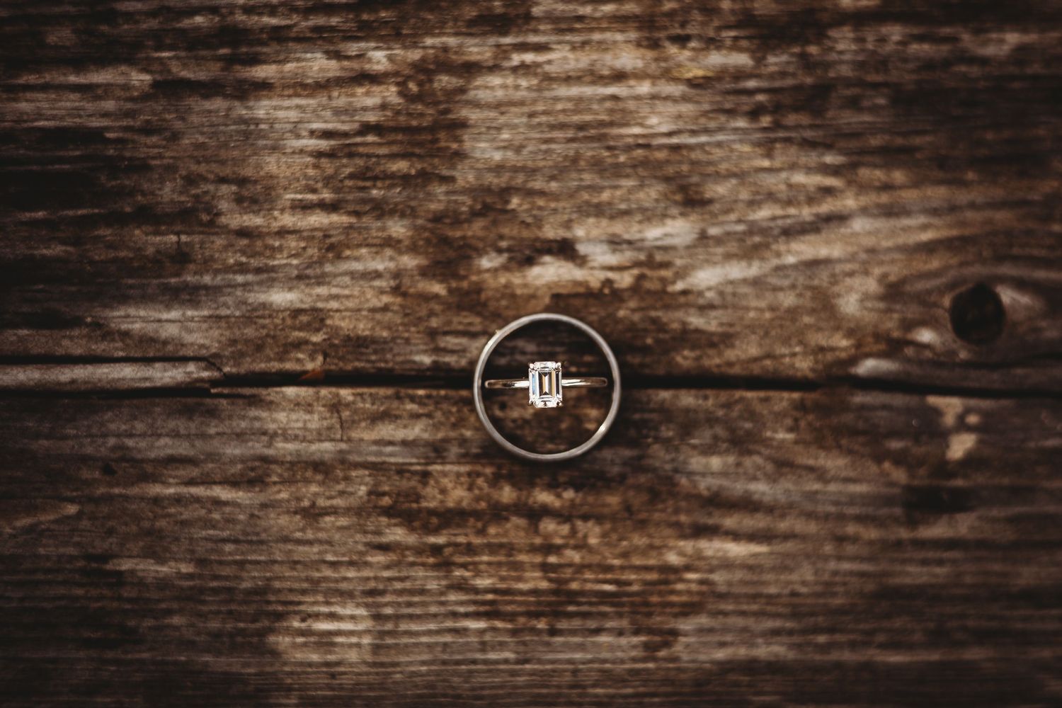 Wedding rings photographed on aged wooden surface with rustic texture.