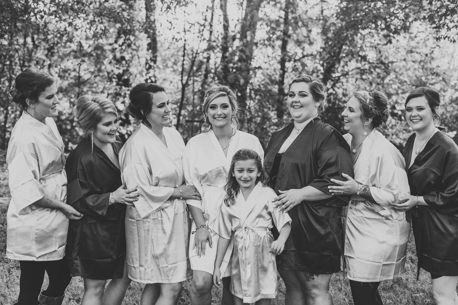 Black and white photo of wedding party in matching robes gathered outdoors.