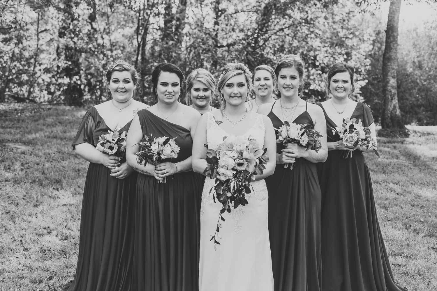 Black and white photo of wedding party in long dresses standing together outdoors.